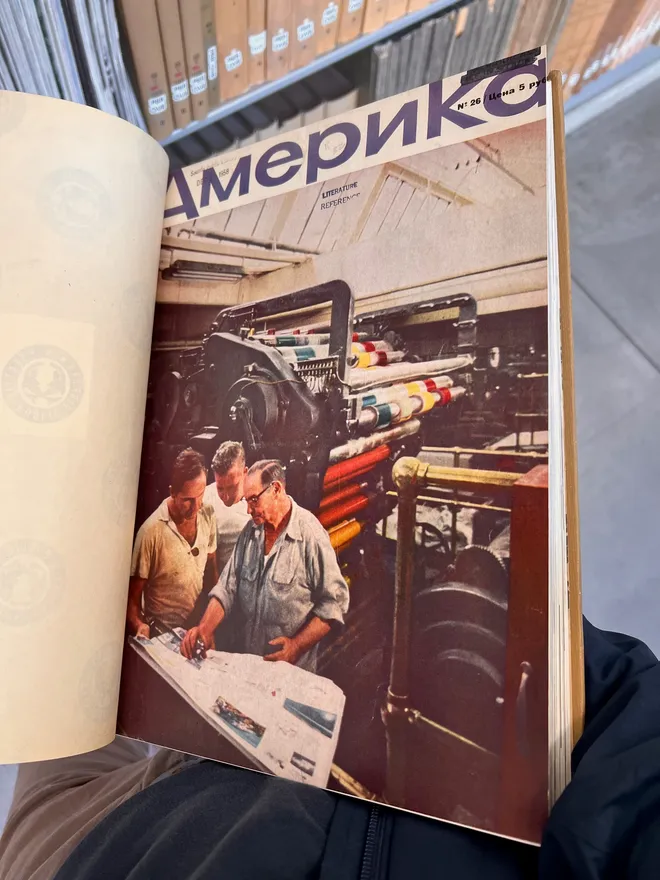 A bound volume open to a cover of Amerika magazine, in Russian, showing three men at a printing press
