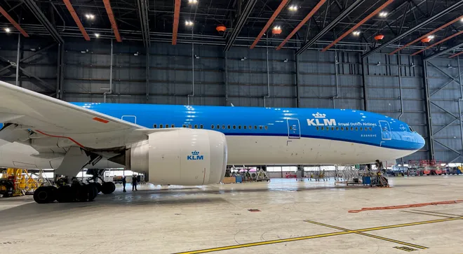 A KLM wide-body jet parked inside a maintenance hangar beneath orange roof beams