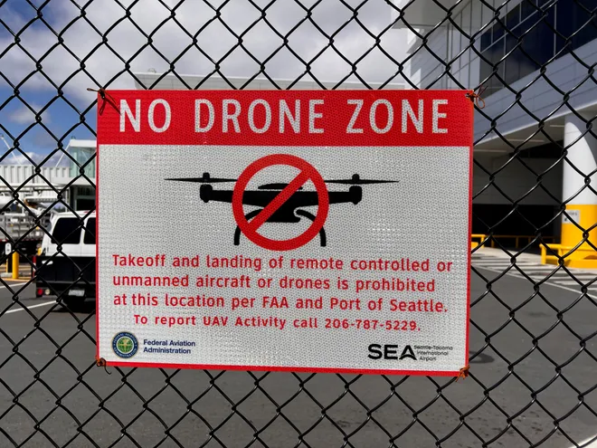 A red and white No Drone Zone sign from the FAA and Port of Seattle, zip-tied to a chain-link fence
