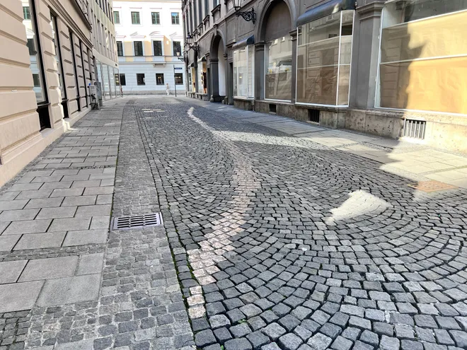 An empty cobbled street, the setts laid in a pale curving line through darker stone